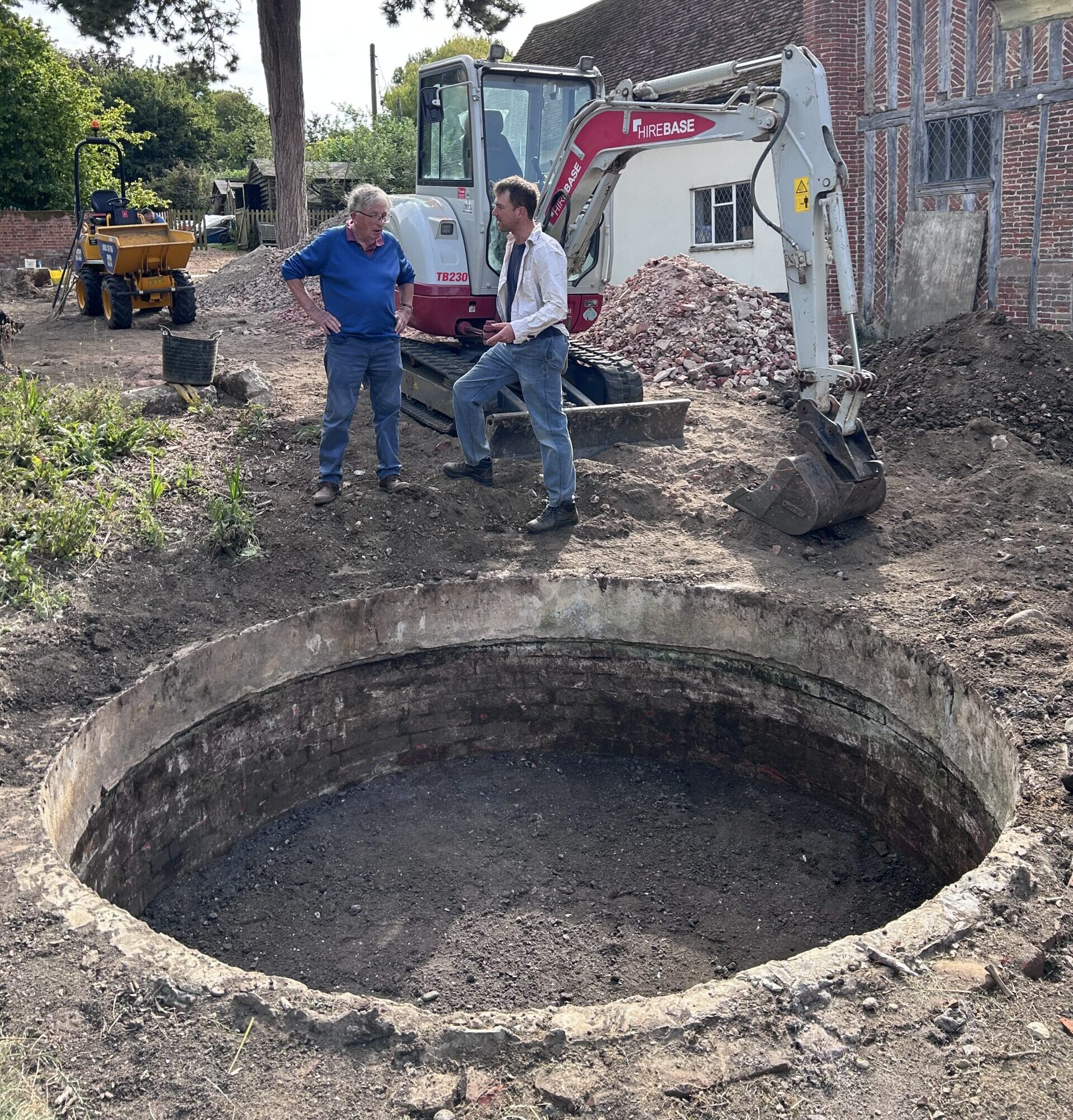 Picture of dug out cistern with two men on other side of it and a digger behind them.